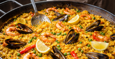Persona cocinando una paella tradicional de mariscos al aire libre, removiendo arroz con gambas, mejillones y limón en una gran paellera sobre fuego de gas