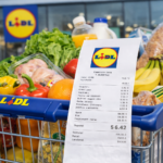 Carrito de supermercado lleno de productos frescos en Lidl con ticket de compra visible en primer plano, mostrando precios y variedad de alimentos como frutas, verduras, pan, leche y carne